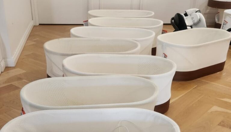 A row of white Snoo smart sleepers lined up in a room with wooden flooring.